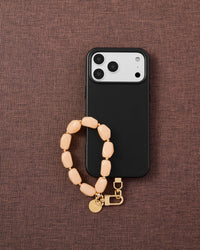 Phone with peach stone strap on dark brown textured fabric lifestyle flat-lay