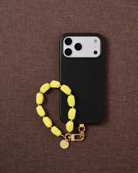 Phone with neon yellow bead strap on dark brown fabric lifestyle flat-lay