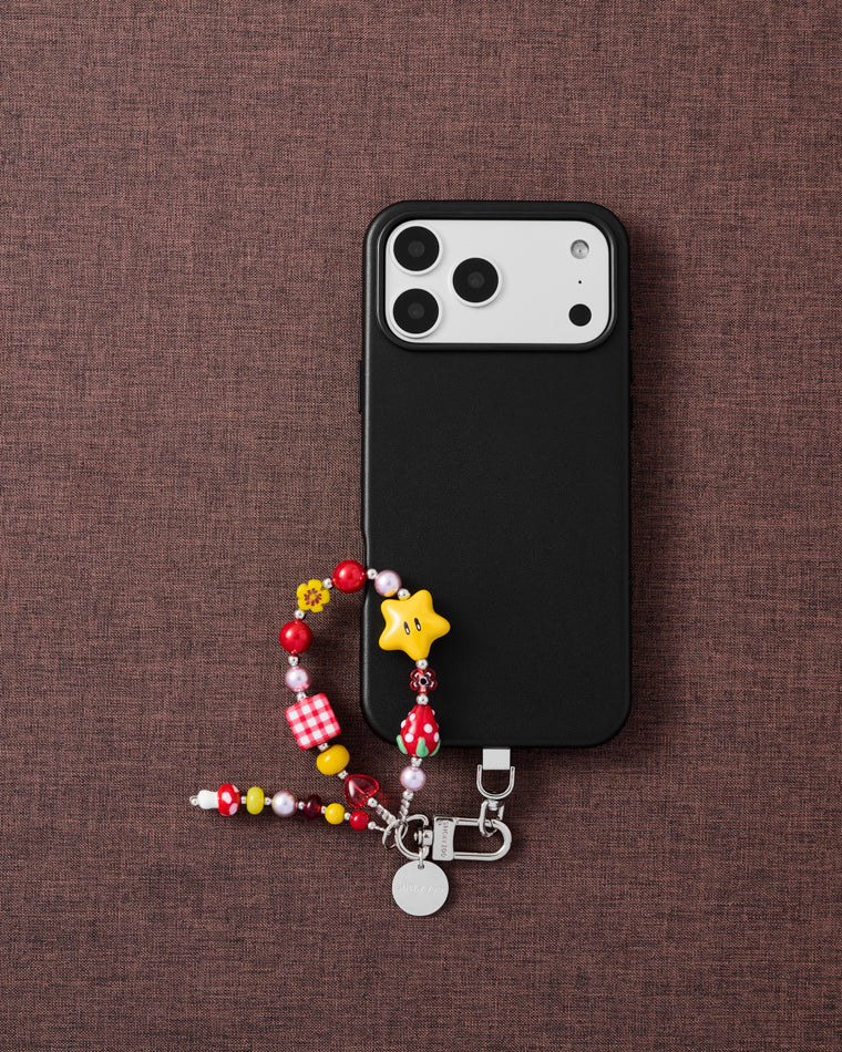 {{Designed in Amsterdam}} Cherry star cluster beaded phone strap with black phone on dark brown fabric lifestyle flat-lay