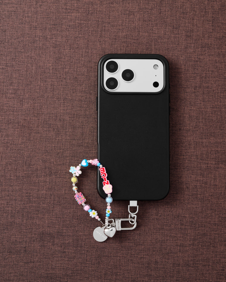 Blush flower cluster phone strap with phone on dark brown fabric lifestyle flat-lay
