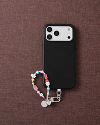 Blush flower cluster phone strap with phone on dark brown fabric lifestyle flat-lay