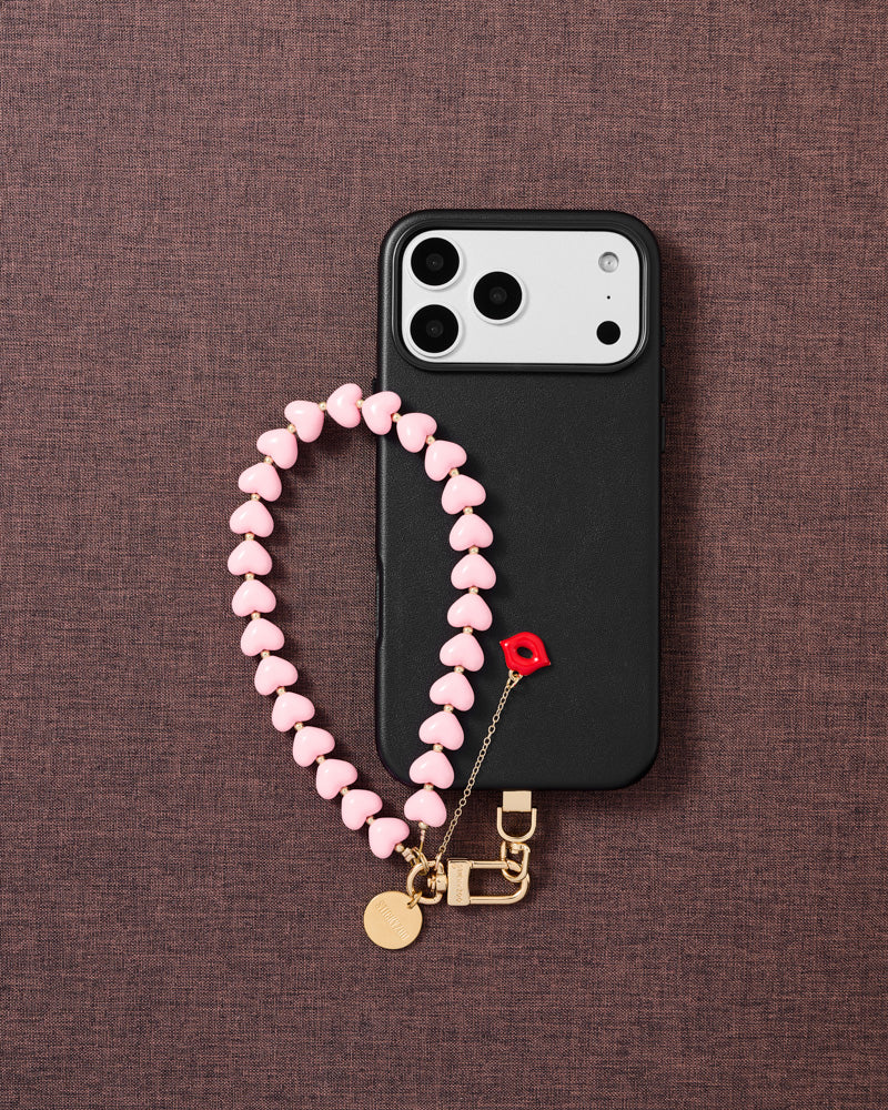 Flat-lay of bubblegum kiss phone strap with engraved gold hardware and Phone Strap Card