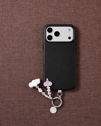 Cloud and pink jelly heart STICKYZOO phone strap laid on brown fabric beside a black phone case, with faux-pearl and faceted iridescent beads.