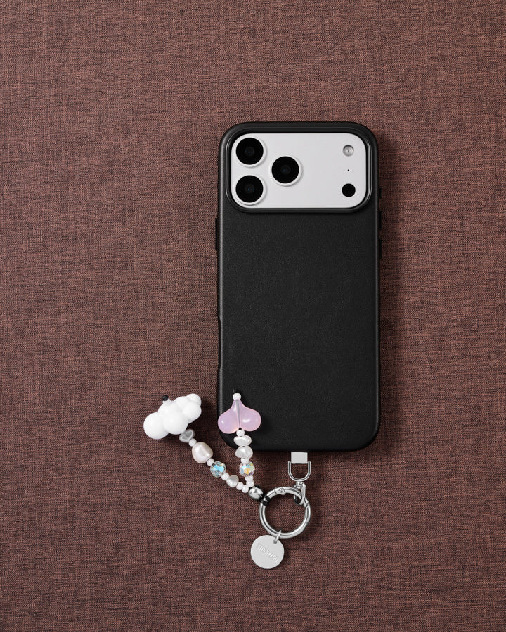 Cloud and pink jelly heart STICKYZOO phone strap laid on brown fabric beside a black phone case, with faux-pearl and faceted iridescent beads.