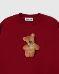 Close-up of plush teddy bear with pearl necklace and ear bow on red cotton sweatshirt showing 3D texture