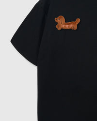 Close-up of hand-stitched plush dachshund on black cotton sleeve showing brown fur texture