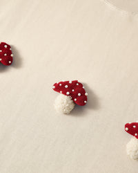 Close-up of plush mushroom applique on cream cotton showing red spotted cap and cream stem