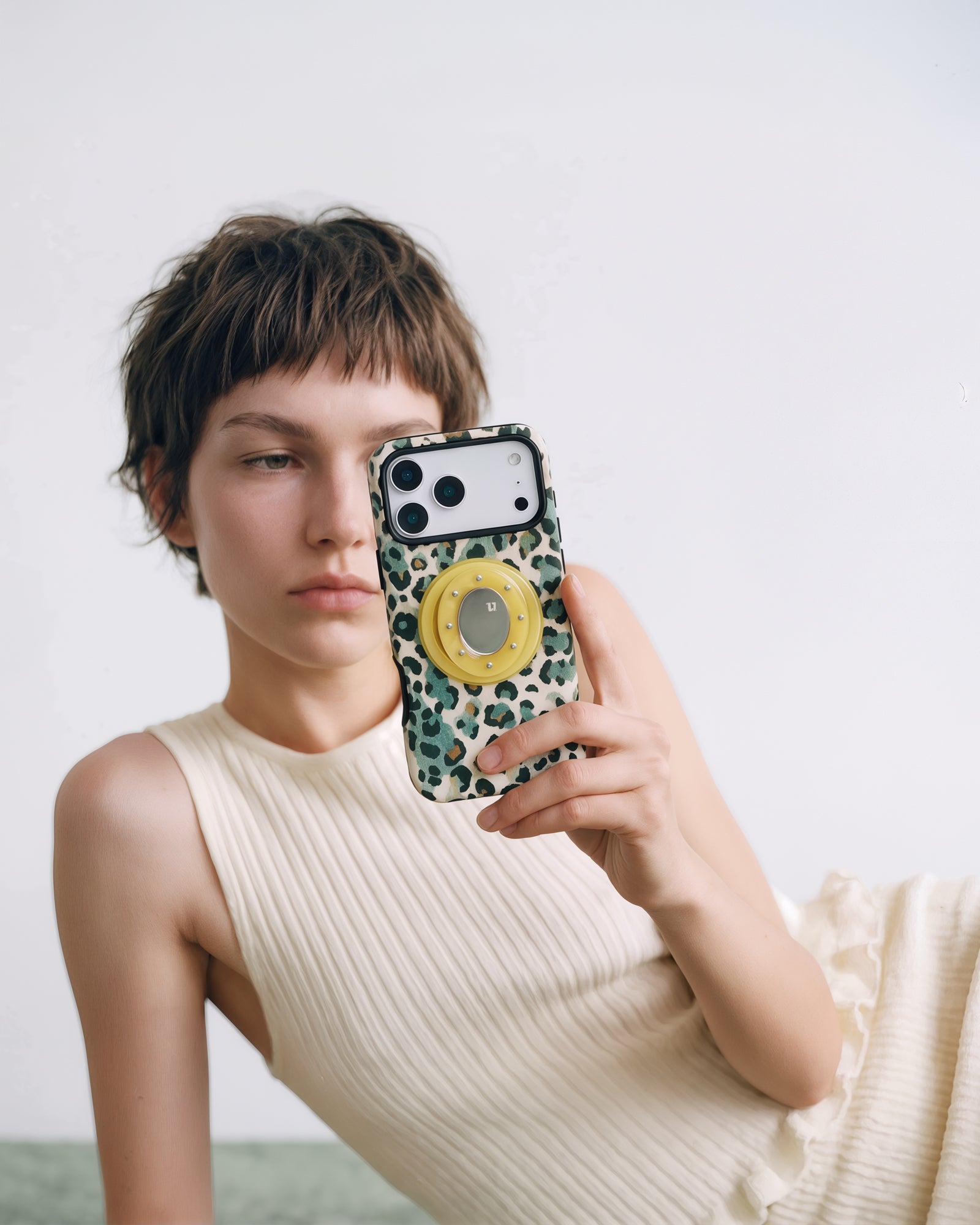 STICKYZOO jade leopard phone case raised for a mirror photo with the MagSafe grip held from behind.