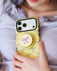 Butter bow phone case held to the chest with the rhinestone-bow grip popped out for an easy hold