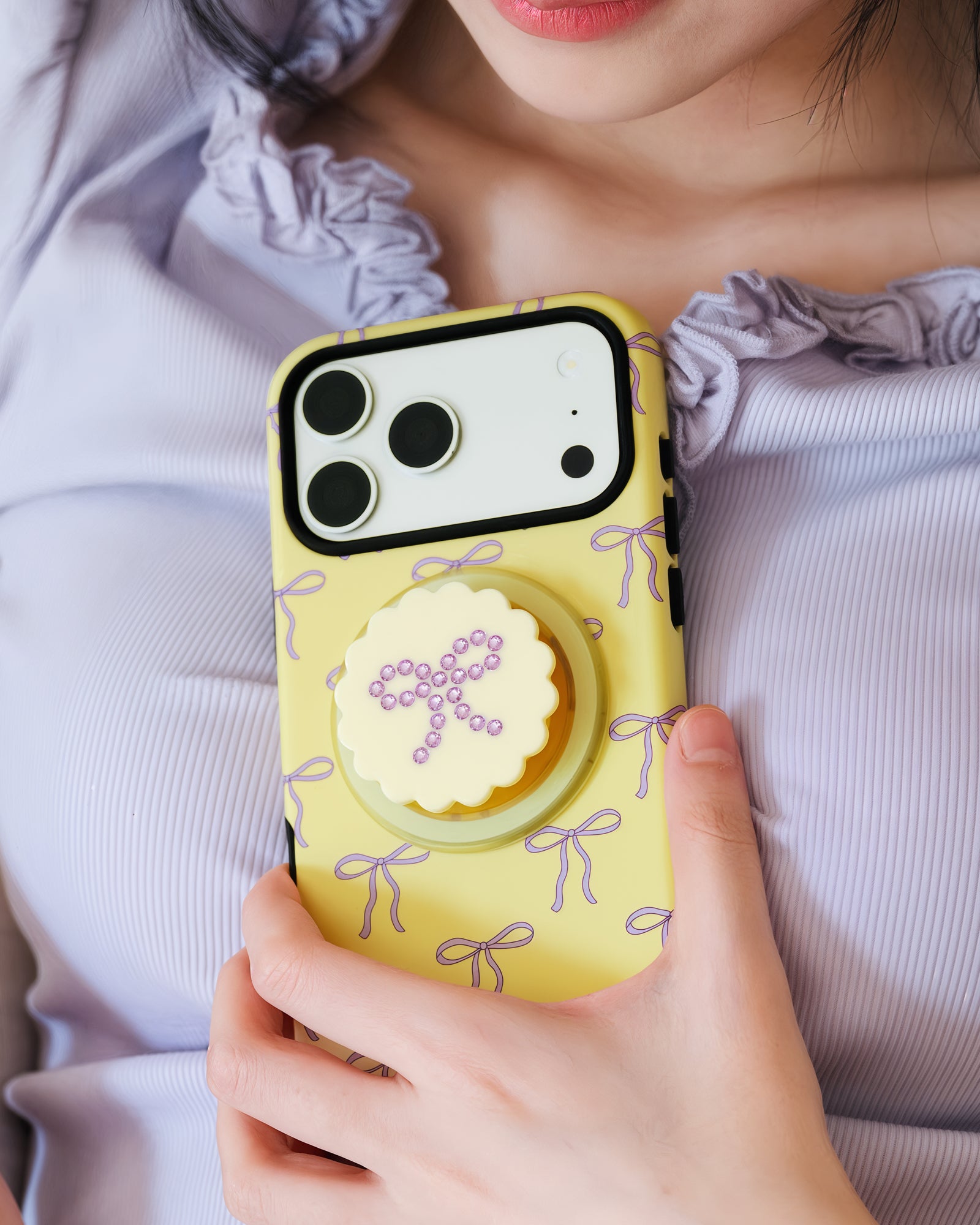Butter bow phone case held to the chest with the rhinestone-bow grip popped out for an easy hold