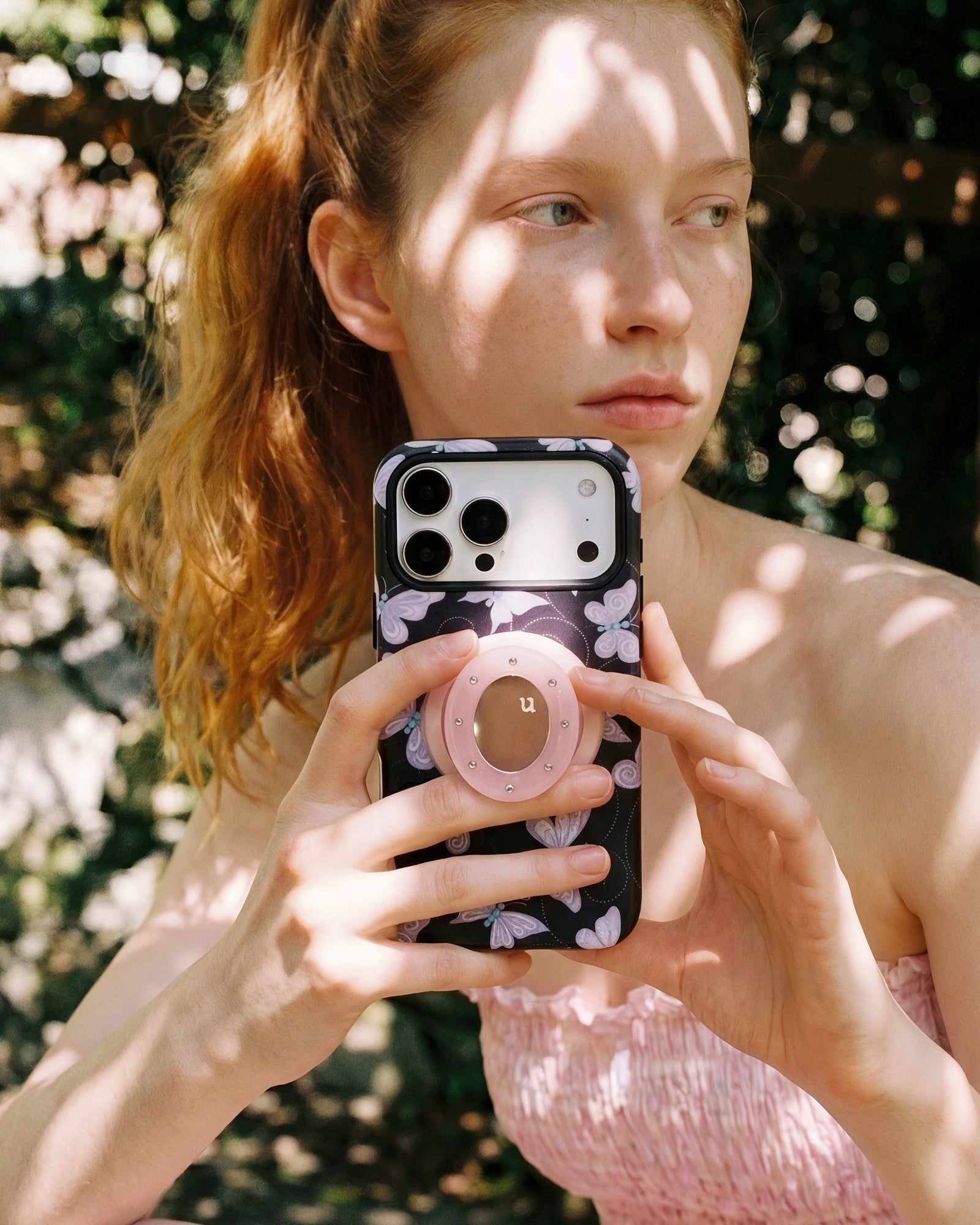 Lavender butterfly phone case held in hand with fingers around the retractable MagSafe grip on the back