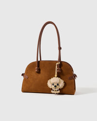 on bag — the poodle charm that earned it. Scalloped alcantara suede curls, 18K gold-plated hardware. 72 hours by hand.