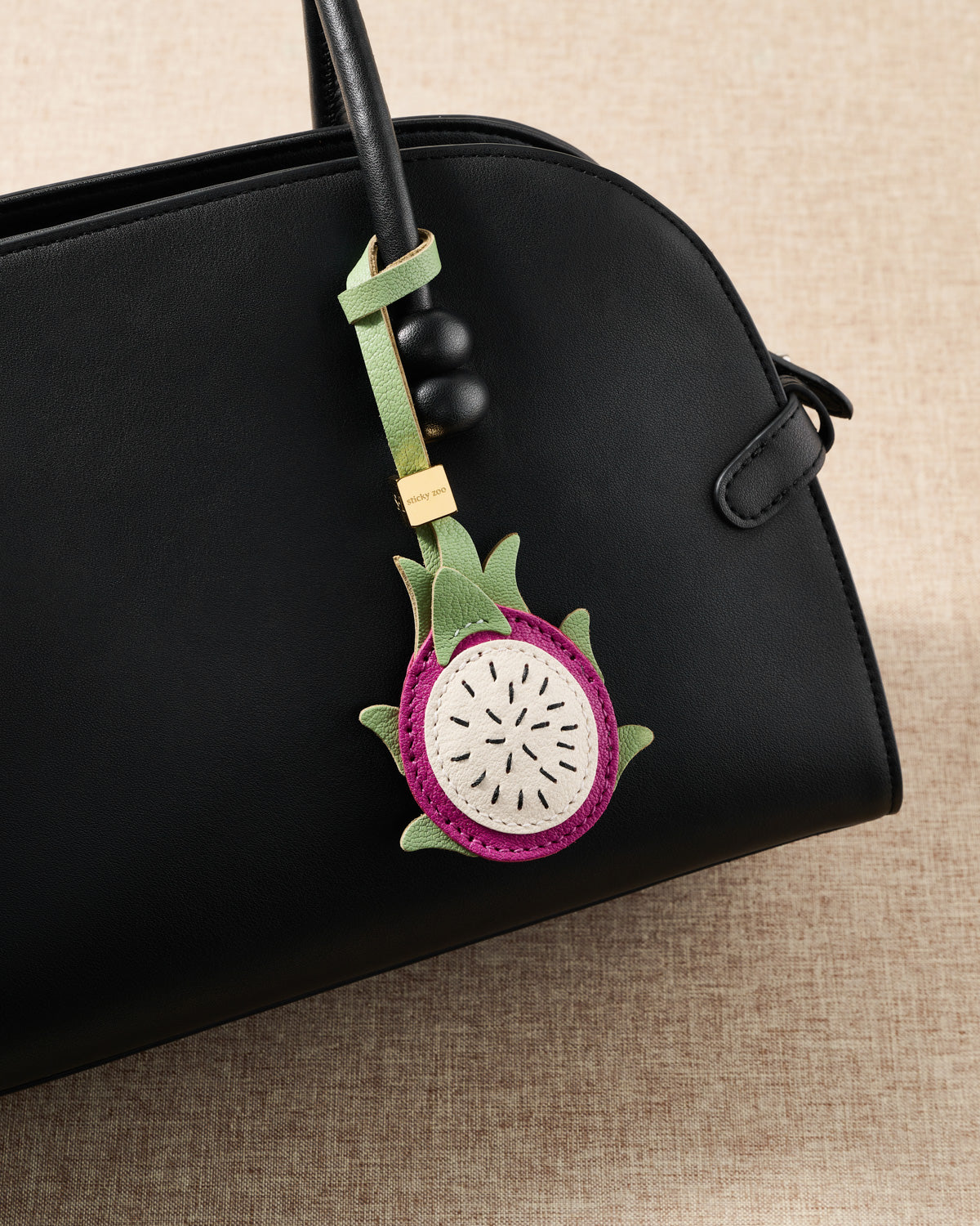Pitaya leather bag charm styled on a black leather handbag showing layered French Alran skin, flesh, and green sepal detail