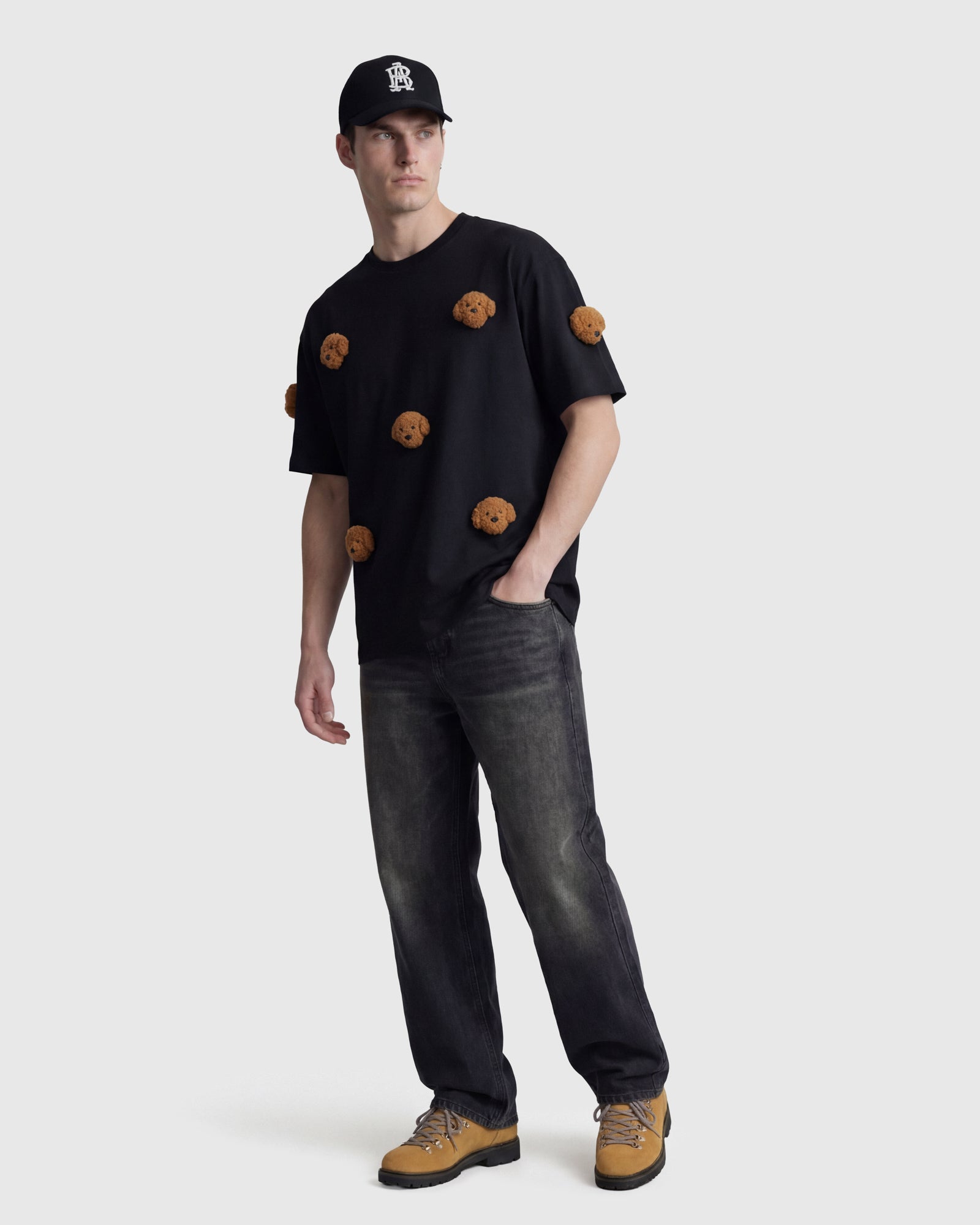 Model wearing STICKYZOO black Poodle Parade T-Shirt with hand in pocket showing plush poodles
