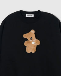 Close-up of plush teddy bear with pearl necklace and ear bow on black cotton sweatshirt showing 3D texture