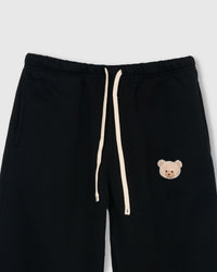 Close-up of check-ear plush teddy bear face on black cotton sweatpant showing gingham ear detail
