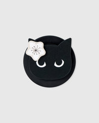 Close-up of the black cat-face medallion with crescent-moon eyes and a white blossom on the acrylic-resin MagSafe grip