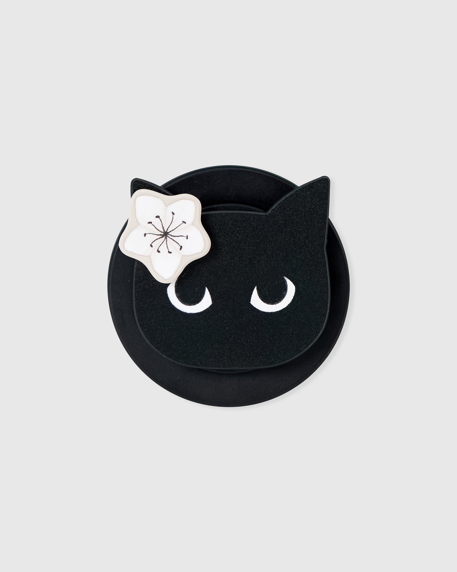 Close-up of the black cat-face medallion with crescent-moon eyes and a white blossom on the acrylic-resin MagSafe grip