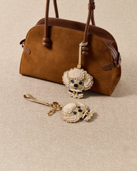 both editions styled together — strap on bag, keychain on linen. Handmade French Alran goatskin and alcantara suede.