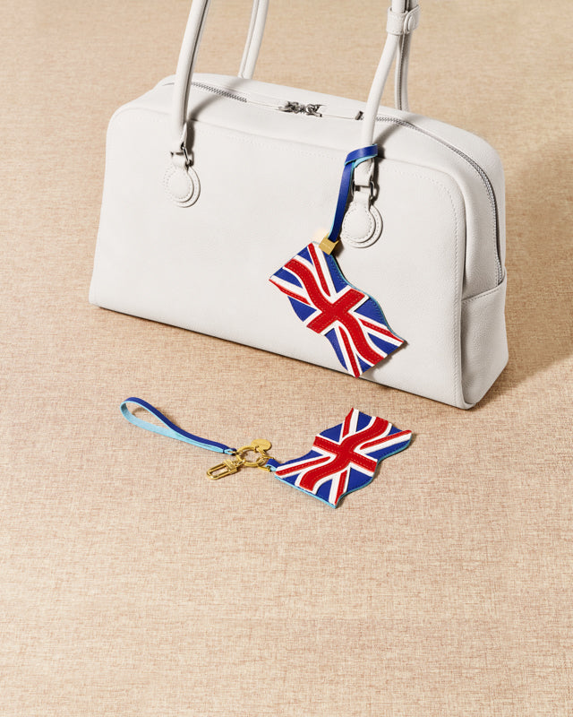 Both Union Jack charm styles — leather strap loop on cream bag and 18K gold-plated keychain clip by STICKYZOO
