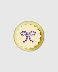 Top-down view of the STICKYZOO grip medallion with its rhinestone bow and yellow polycarbonate MagSafe ring base