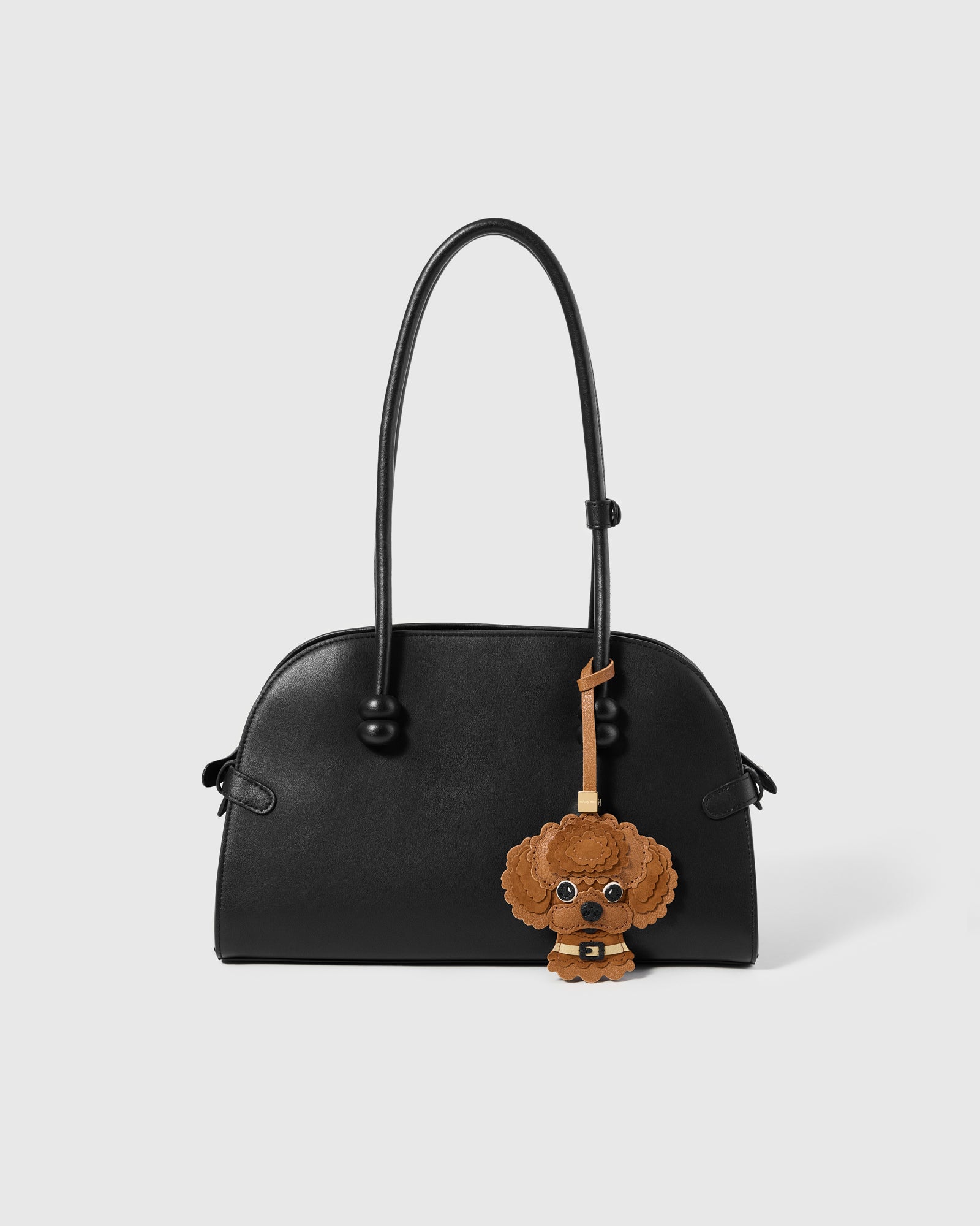 {{The exclusive drop.}} The Poodle Charm styled on a glossy black top-handle bag, front — Alcantara curls and French Alran leather against dark leather. Limited availability.