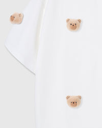Detail of hand-stitched bear faces scattered across white cotton showing dimensional construction