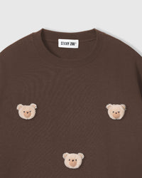 Close-up of plush bear face applique on brown cotton showing checkered ear and beige fur detail