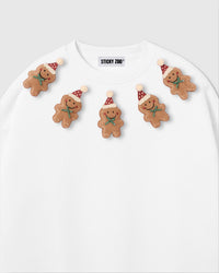 Close-up of plush gingerbread men on white sweatshirt showing Santa hats and green bow detail