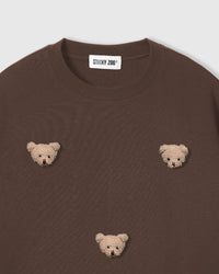 Close-up of plush bear face appliques on brown 230gsm cotton showing fuzzy 3D texture and embroidered features