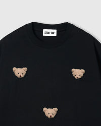 Close-up of plush bear face appliques on black 230gsm cotton showing fuzzy 3D texture and embroidered features