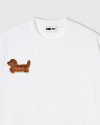 Close-up of plush dachshund applique on white cotton showing brown fur texture and dimensional stitching
