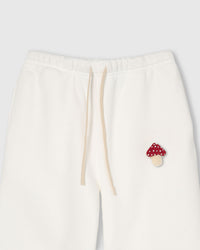 Detail view of plush mushroom applique near elastic drawstring waistband on cream sweatpant