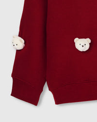 Close-up of white plush bears near lower hem and sleeve on red cotton