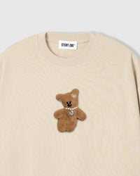 Close-up of plush teddy bear applique on cream cotton showing fur texture and pearl detail