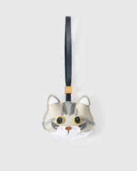 Silver Tabby American Shorthair cat charm handmade from French Alran genuine goatskin — cream-grey body, darker silver tabby markings, gold eyes, copper heart nose, black leather strap. Three days by hand. Arrives in luxury gift packaging. Designed in Amsterdam.