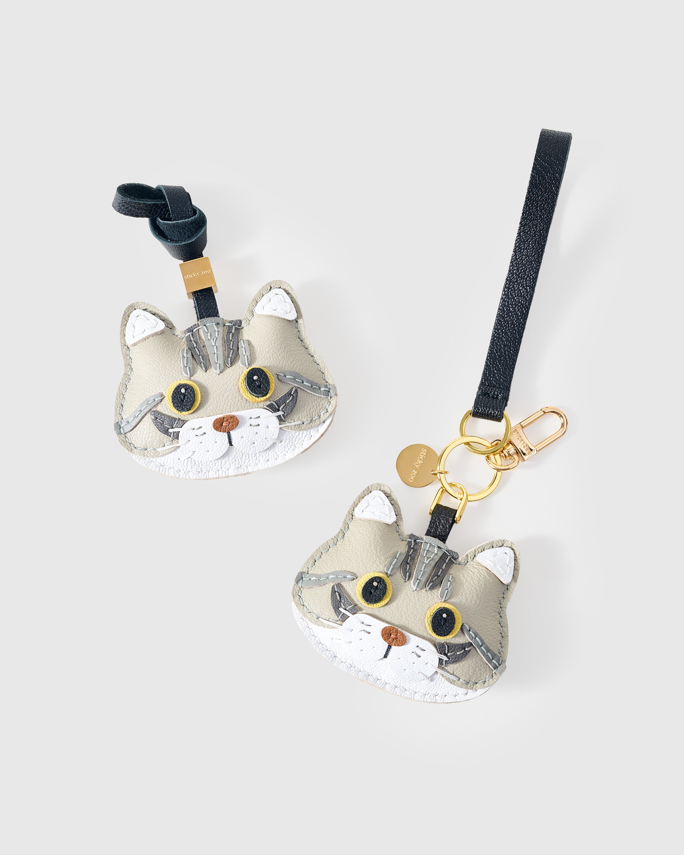 {{Dual attachment.}} Both editions of the Silver Tabby American Shorthair side by side — leather strap loop for bags, or 18K gold-plated keychain clip.