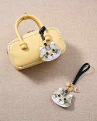 Overhead — Silver Tabby American Shorthair in strap and keychain editions alongside a soft-yellow box bag. Finished one at a time, by hand.