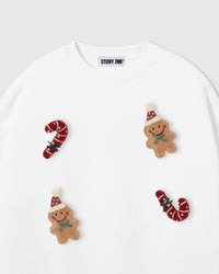 Close-up of scattered plush appliques on white sweatshirt showing gingerbread men and candy cane 3D texture