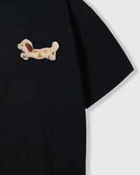 Close-up of spotted dachshund plush on shoulder area of black tee showing plush detail