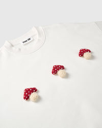Angled close-up of three hand-stitched 3D plush mushrooms scattered across cream cotton