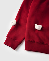Close-up of white plush bear faces at sleeve cuff showing ribbed trim on red cotton