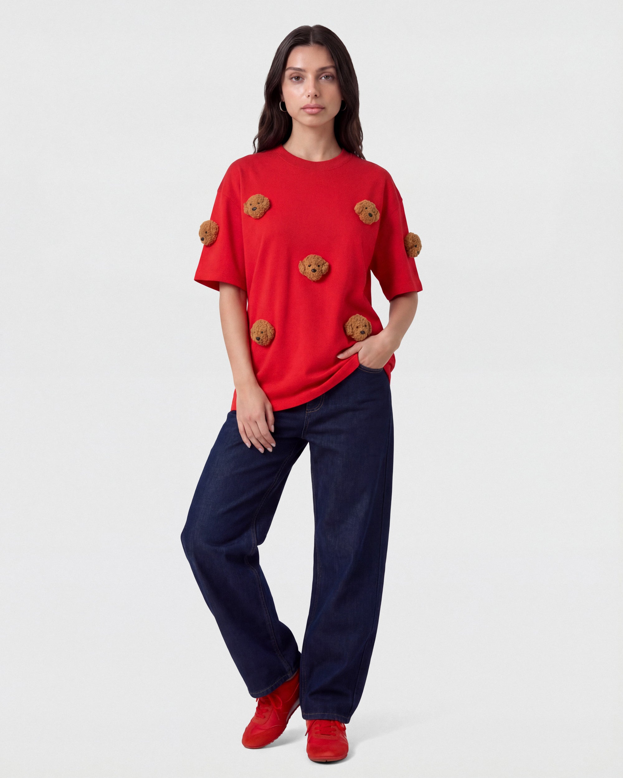 {{Not printed — stitched}} Model styling red Poodle Parade T-Shirt with hands in pockets showing relaxed silhouette