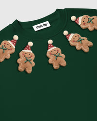 Close-up of plush gingerbread men on forest green sweatshirt showing polka-dot hats and green bows