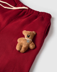 Close-up of full-body plush teddy bear applique on red cotton showing pearl necklace and pendant detail