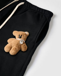 Close-up of plush teddy bear with pearl necklace on black cotton sweatpant showing 3D texture