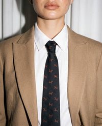 Designed in Amsterdam Model in tan blazer wearing STICKYZOO Dachshund Tie, arms crossed, showing tie knot and embroidered dachshund detail