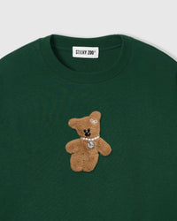 Close-up of plush teddy bear applique showing brown fur texture, pearl necklace, and pendant detail