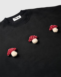 Angled close-up of three hand-stitched 3D plush mushrooms on black cotton showing dimensional texture