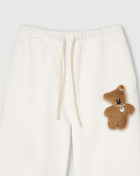 Close-up of waistband area showing full-body plush teddy bear with pearl necklace on white cotton